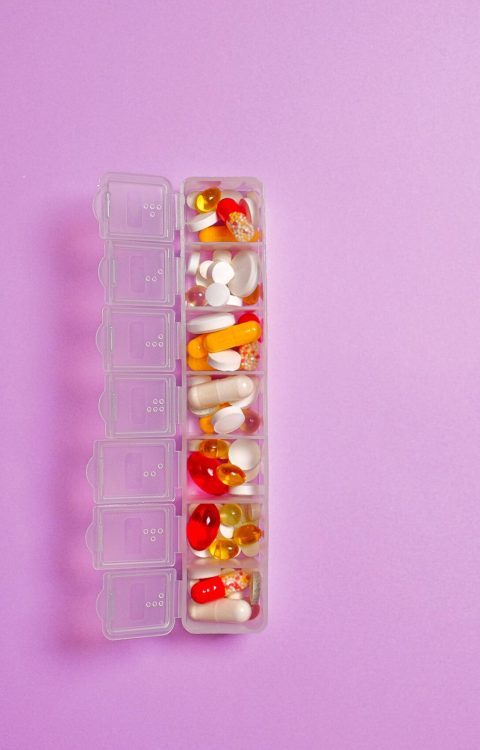 Close-up of assorted pills in a weekly organizer against a violet background.